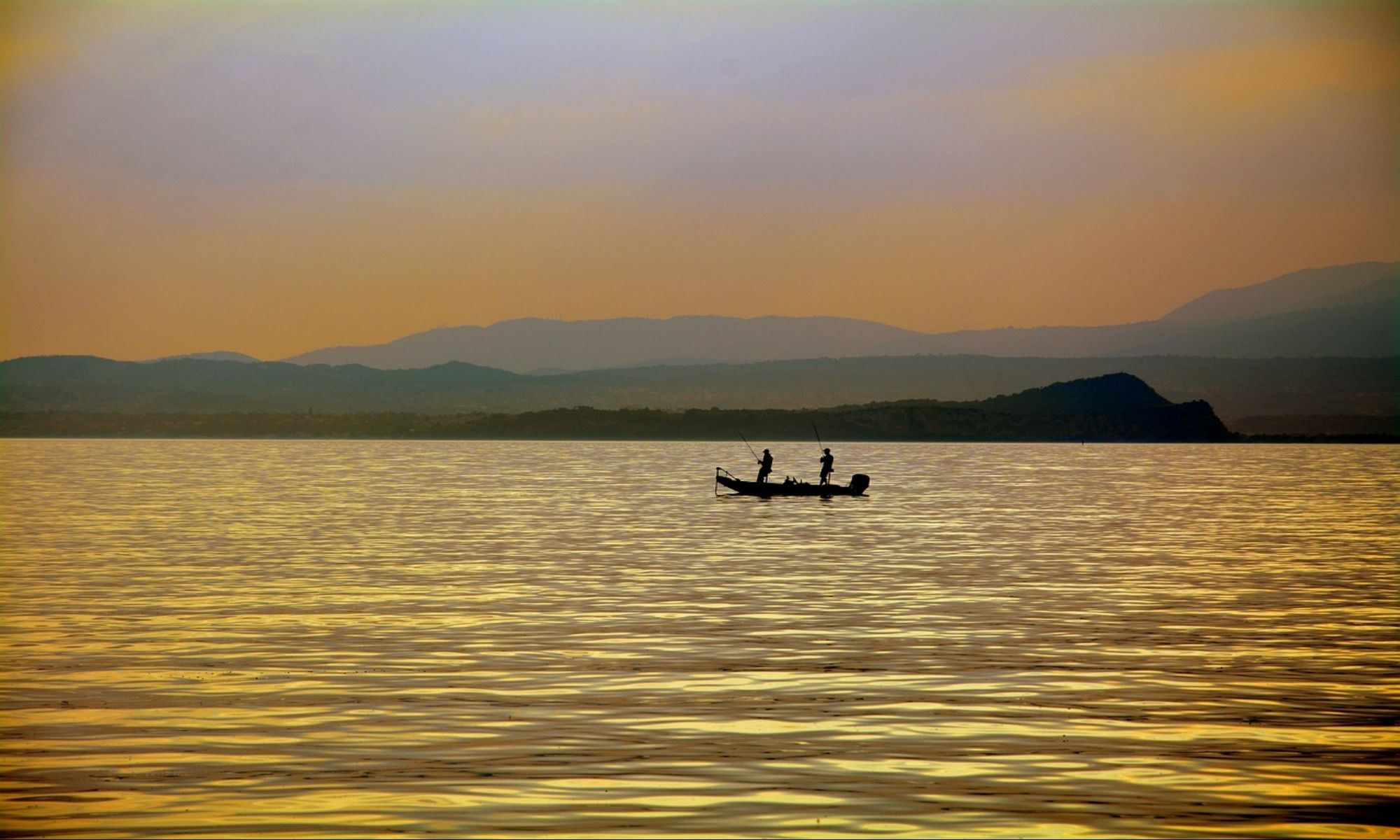 two people on a boat fishing during sunset