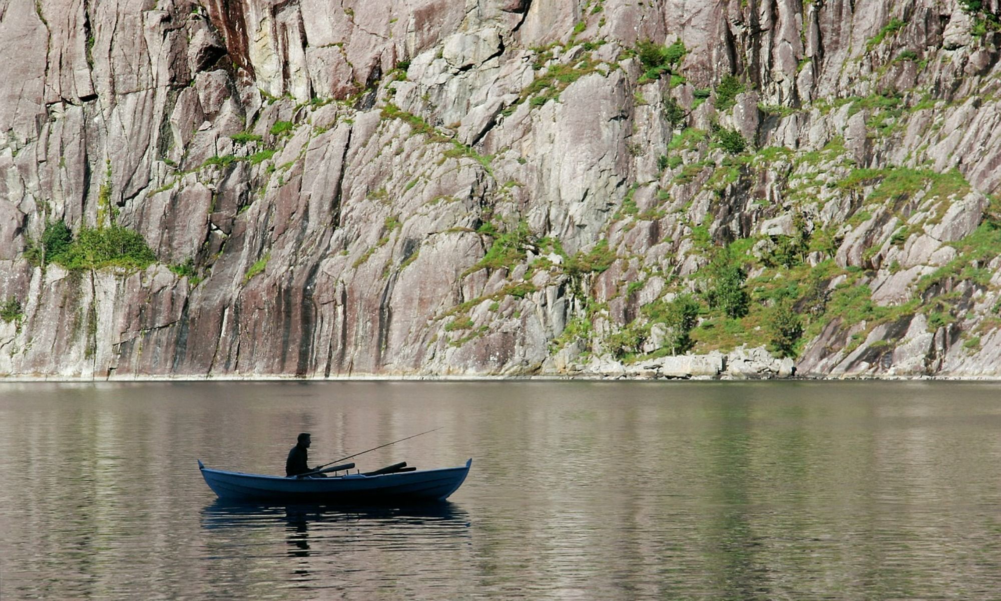 person on a boat holding a fishing rod fishing by the lake 