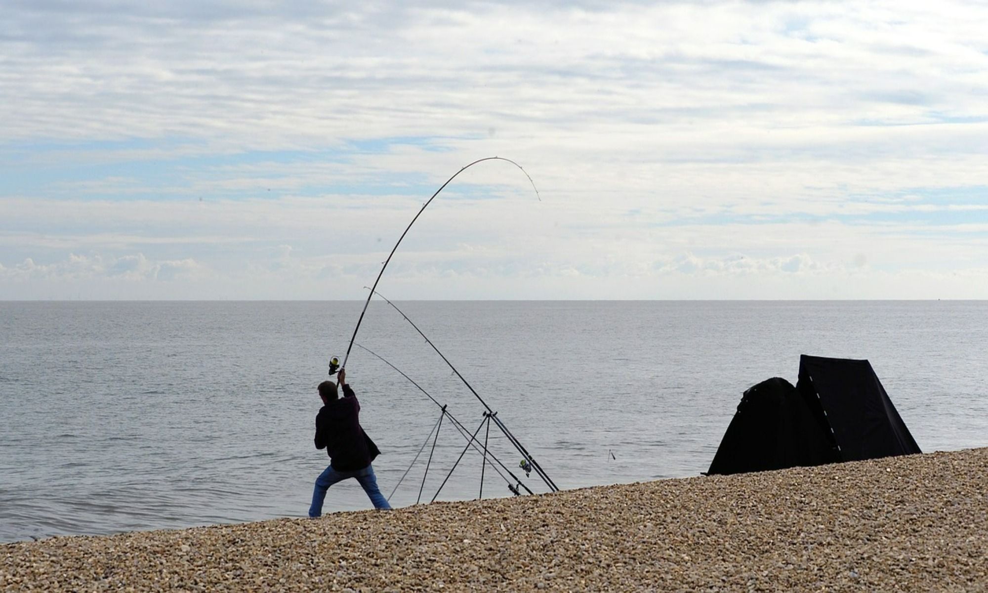 man casting a fishing rod beside his black tent