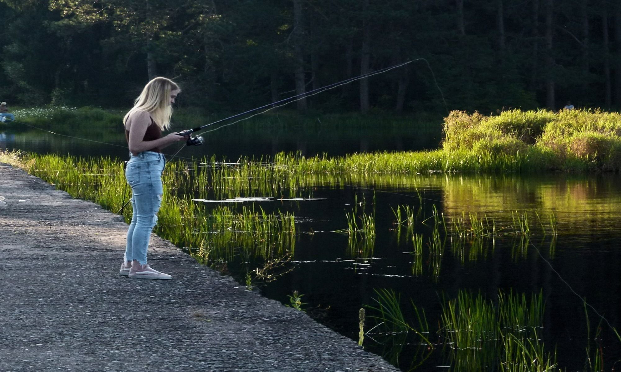 young woman wearing black top fishing by the lake