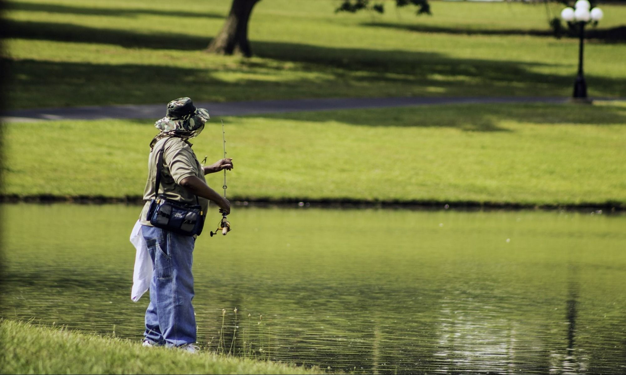 man wearing a bucket hat and holding a fishing rod near pond